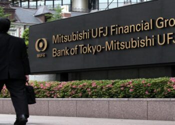 Businessmen walk past a sign at the headquarters of the Bank of Tokyo-Mitsubishi UFJ Ltd. in Tokyo, Japan, on Monday, May 16, 2011. Mitsubishi UFJ Financial Group Inc., Japan's biggest bank, targeted a 2.9 percent profit increase this year after a recovery at its consumer lending unit and the slated conversion of Morgan Stanley preferred shares. Photographer: Kimimasa Mayama/Bloomberg