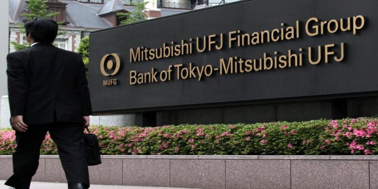 Businessmen walk past a sign at the headquarters of the Bank of Tokyo-Mitsubishi UFJ Ltd. in Tokyo, Japan, on Monday, May 16, 2011. Mitsubishi UFJ Financial Group Inc., Japan's biggest bank, targeted a 2.9 percent profit increase this year after a recovery at its consumer lending unit and the slated conversion of Morgan Stanley preferred shares. Photographer: Kimimasa Mayama/Bloomberg